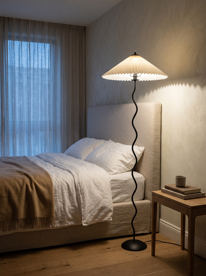 Dune floor lamp beside a linen-dressed bed at dusk